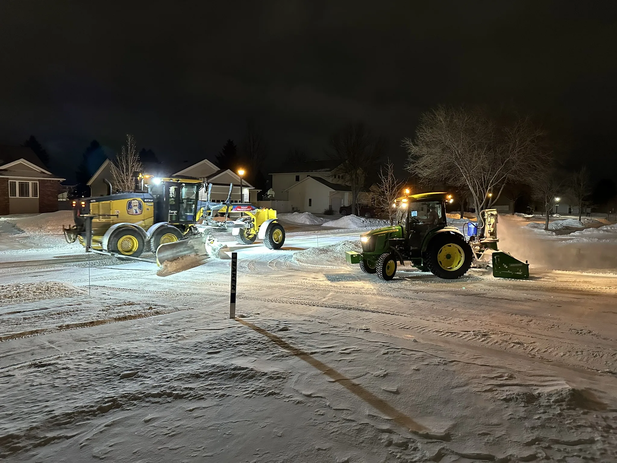 A Baker Snow & Ice tractor with inverted snowblower alongside a city plow truck